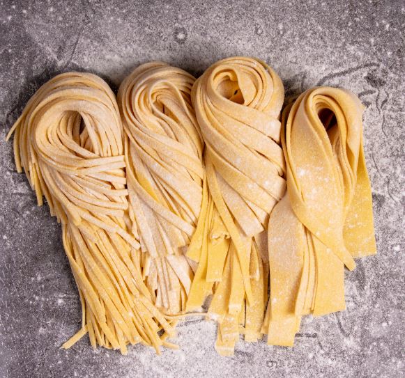 Four freshly rolled durum pasta styles cut into different lengths on floured bench at Maria's Pasta