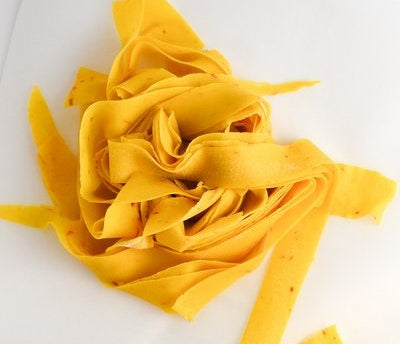 Saffron pasta sliced into ribbons on white bench